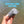 A hand holding a gray cylindrical line waste holder and cutter with a metal keyring, set against a background of shallow water, with the text 'BUILT-IN LINE CUTTER' at the top.