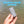 A hand holding a gray cylindrical outdoor accessory with a metal key ring, set against a background of water with a blue text overlay reading 'MULTIPLE COLOR OPTIONS'.