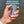 A hand holding a gray cylindrical fishing line waste holder over water, with the text 'RUST-PROOF AND DURABLE' in blue at the top.