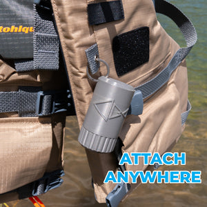 A gray cylindrical waste fishing line holder, attached to a tan vest strap in shallow water. The text 'ATTACH ANYWHERE' is overlaid in blue on the bottom right.