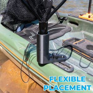A black fishing net and net holder attached to the side of a green kayak on water, with a net hanging above it. Large blue text at the bottom right reads 'FLEXIBLE PLACEMENT'.