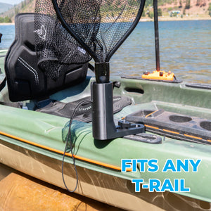 A black fishing net holder attached to the side of a green kayak in a lake setting, with a fishing net and seat visible. Blue text overlay reads 'FITS ANY T-RAIL'.