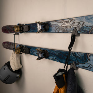 Pair of skis with bindings attached to a wall, with a helmet and gloves hanging below.