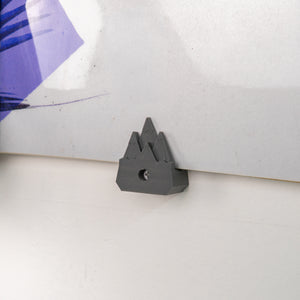 Close-up of a gray plastic holder on a white surface with a purple snowboard in the background.