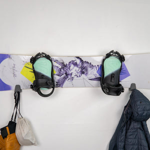 Colorful snowboard with bindings on a white surface, surrounded by winter gear.
