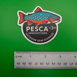 Brook trout and 'PESCA Innovations' sticker on a green background, accompanied by a ruler for scale, 3 inches wide