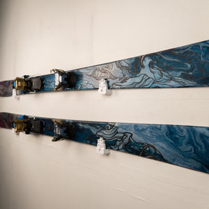 Two pairs of marbled blue and gray skis with bindings on a white wall.
