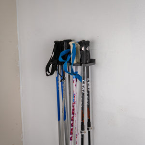 Set of ski poles with attachments on a wall-mounted holder against a white wall.