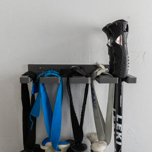 Wall-mounted rack with various items including ski poles and straps against a white wall.