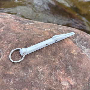 White keychain with a small tool on a rock by a water source
